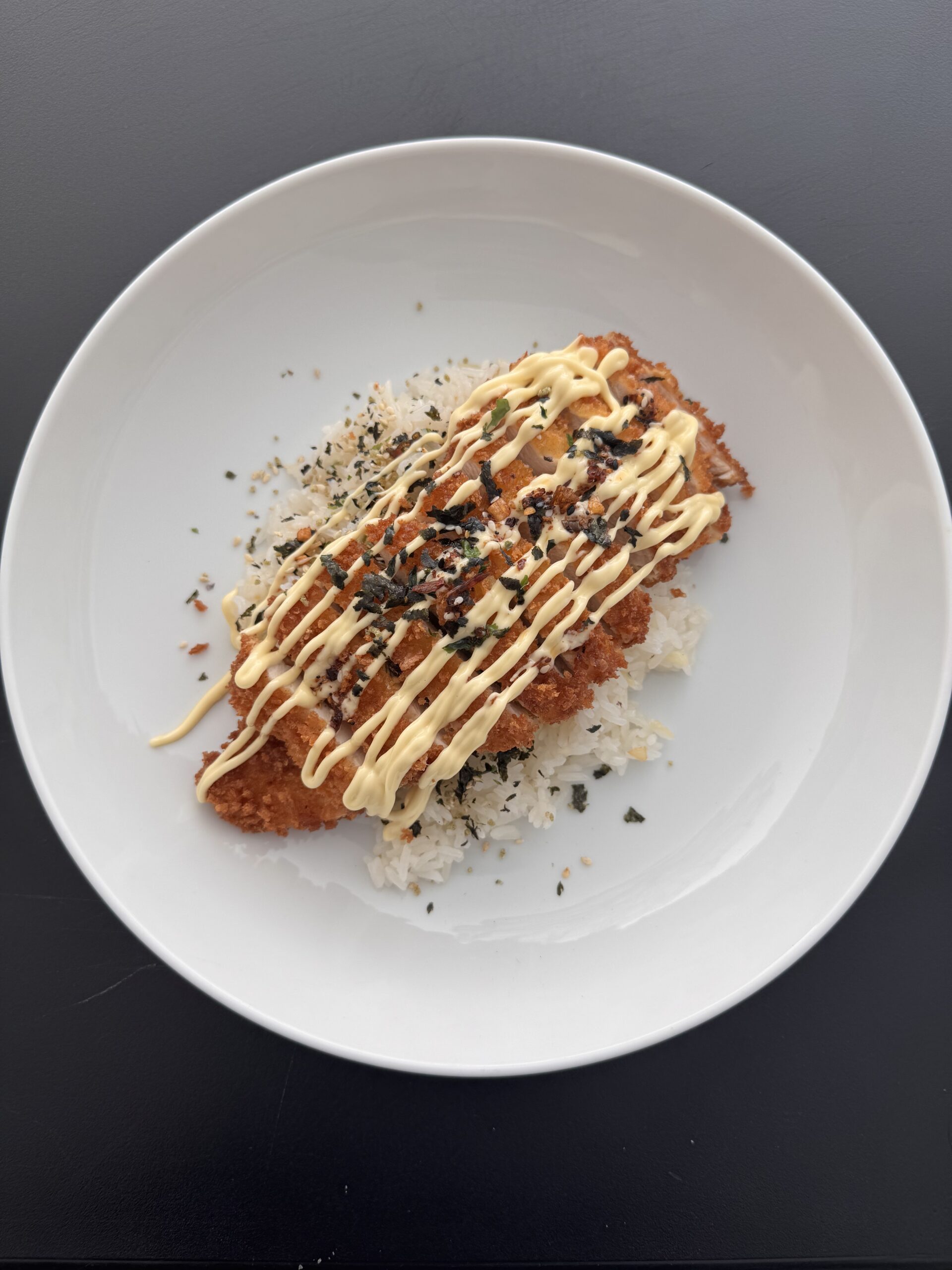 A plate of crispy, golden chicken katsu sliced over white rice, drizzled with creamy sauce and topped with furikake seasoning, prepared by Gen's Luncheonette in Cathedral City.
